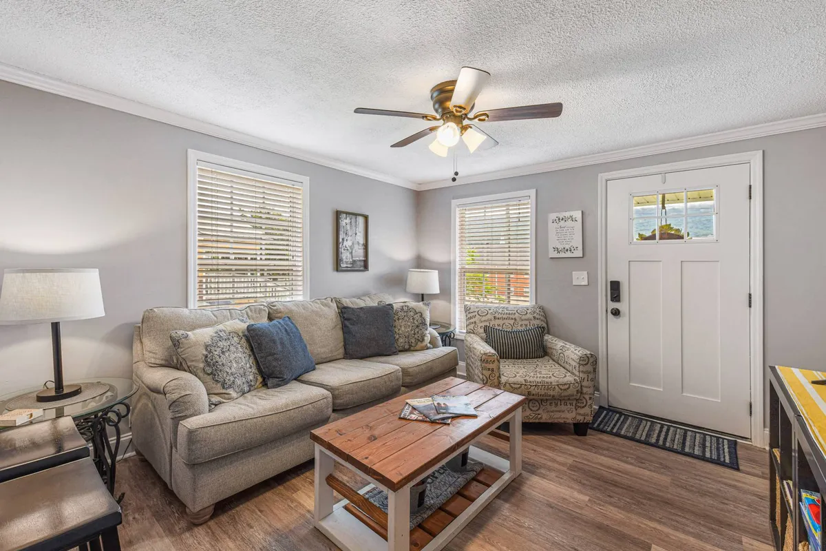 A cozy living area featuring a sofa with decorative pillows, a wooden coffee table, a comfortable chair, and the front door with a window that allows in natural light. The room is inviting with warm tones and tasteful decor, creating a welcoming atmosphere right at the entry.