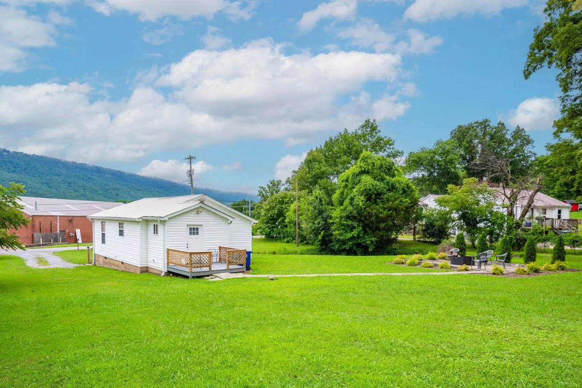 The image showcases the charming exterior of a single-family house set against a lush green lawn and a stunning mountain backdrop. A spacious deck invites relaxation and gatherings, while the peaceful garden setting radiates tranquility, all bathed in the warm glow of sunset.