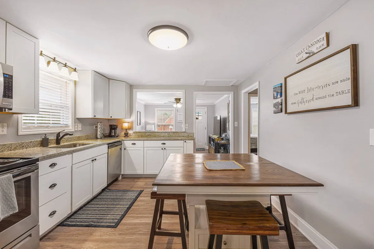 A bright, modern kitchen featuring a spacious kitchen island, gleaming quartz countertops, and stainless steel appliances. Natural light streams in from the window, illuminating the inviting space. The countertops are set with cookware and essentials, creating a functional and attractive area for meal preparation.