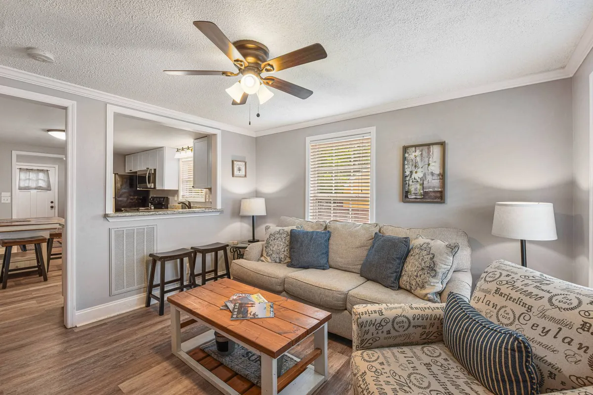 A cozy living area featuring a plush sofa, coffee table, ceiling fan, and artwork on the wall. The space is warmly lit and designed for comfortable relaxation and socializing, capturing a welcoming atmosphere ideal for gatherings.