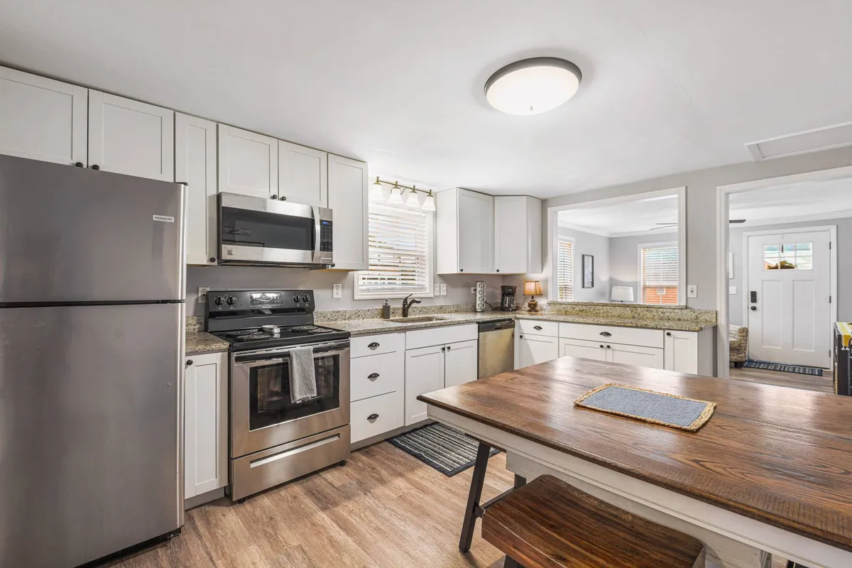 A bright and well-equipped kitchen with stainless steel appliances, a sturdy wooden dining table, granite countertops, and large windows that bathe the space in natural light. The kitchen is set up for cooking, family meals, and entertaining guests.