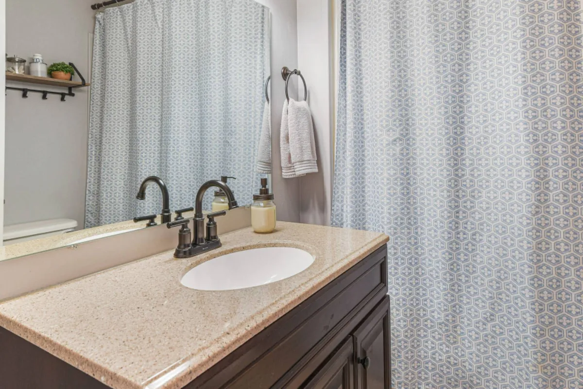 A calm bathroom space featuring a vanity, mirror, and shower curtain. The area is tidy, well-lit, and designed for relaxation and self-care, evoking a sense of tranquility and cleanliness.