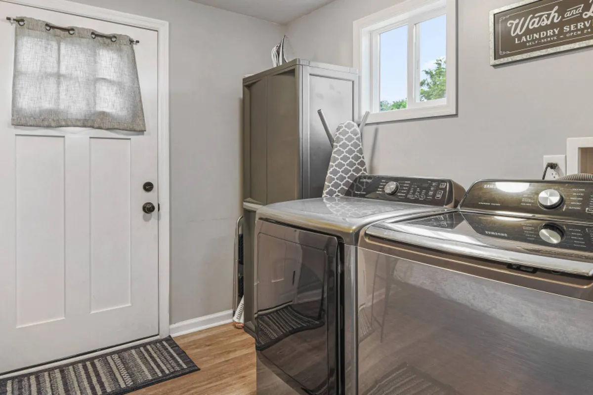 A practical laundry area with a washing machine, dryer, front door, and window. The space is tidy and organized, making it perfect for laundry tasks or preparing for extended stays.
